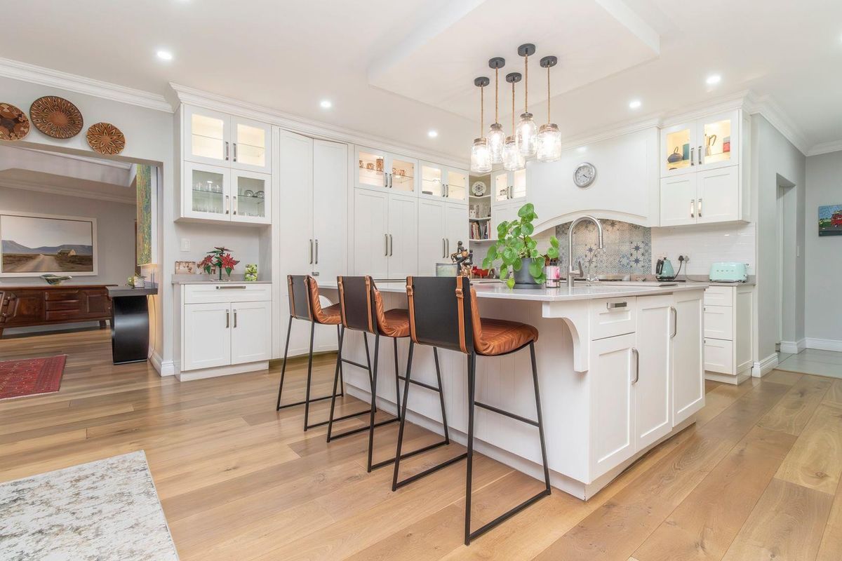 A modern, well-appointed kitchen featuring white cabinetry, a central island with seating, hardwood flooring, and elegant pendant lighting.