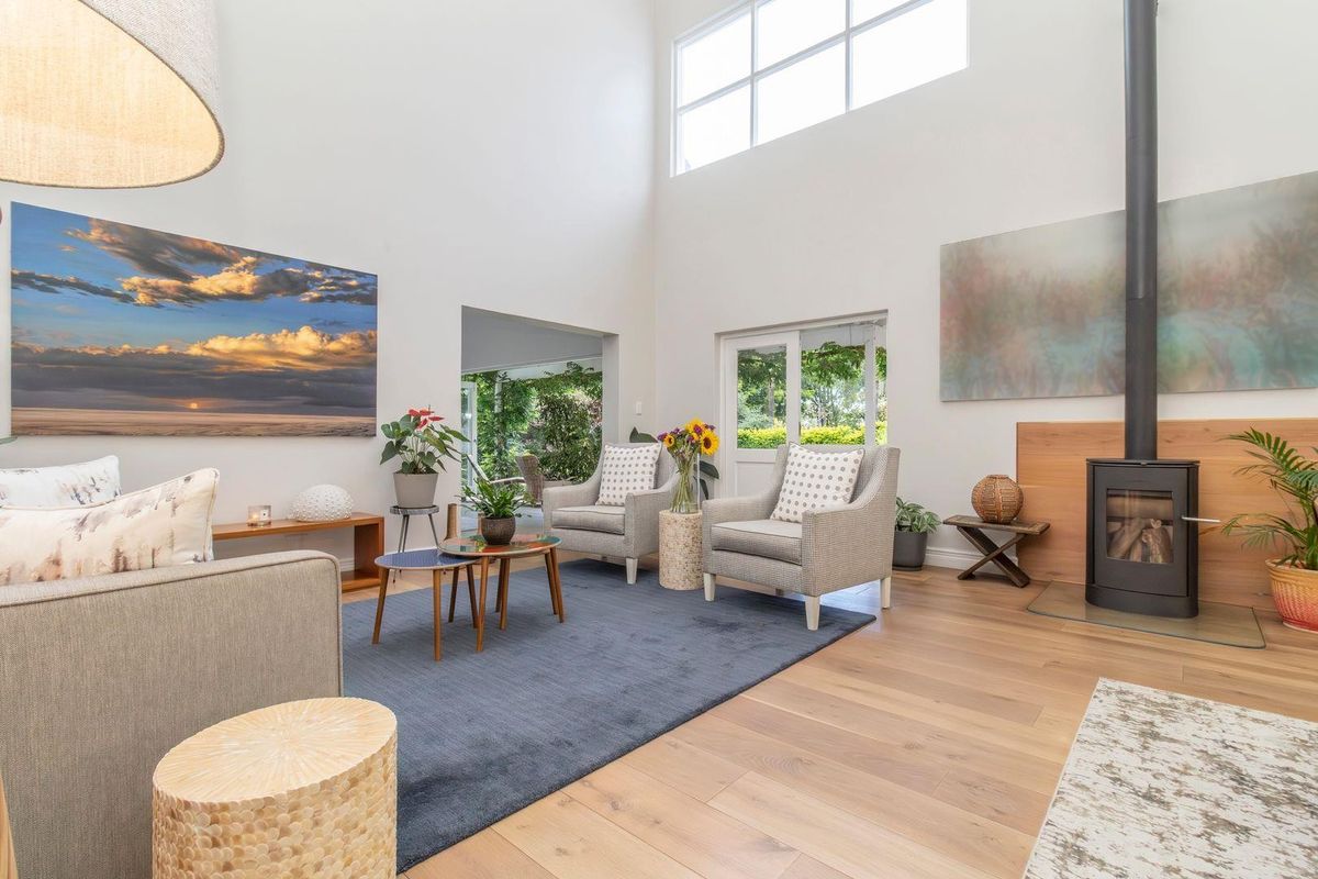 Spacious living room featuring high ceilings, timber flooring, and a modern freestanding fireplace, with large windows providing ample natural light and garden access.