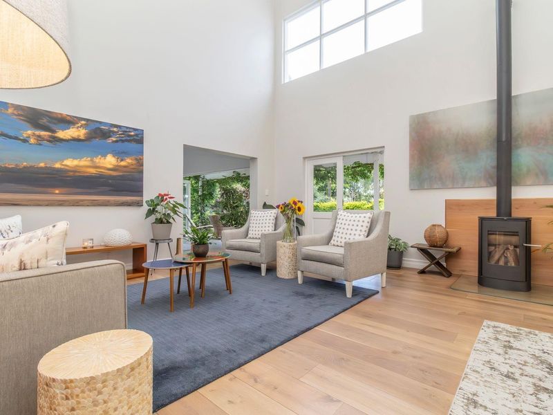 Spacious living room featuring high ceilings, timber flooring, and a modern freestanding fireplace, with large windows providing ample natural light and garden access.