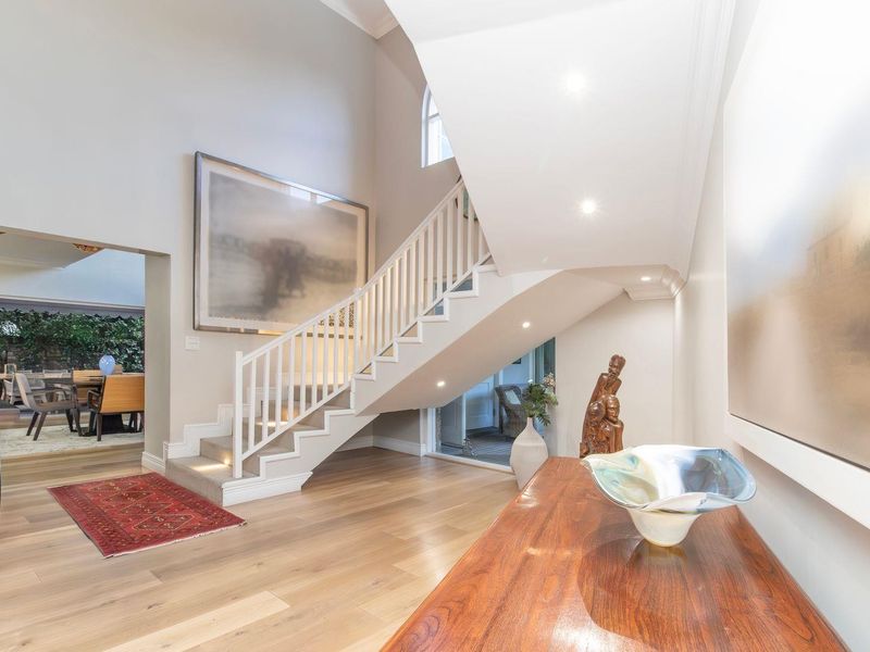 Spacious double-volume entrance hall featuring elegant timber flooring, a modern staircase with white balustrades, and recessed lighting, leading into the open-plan living areas.