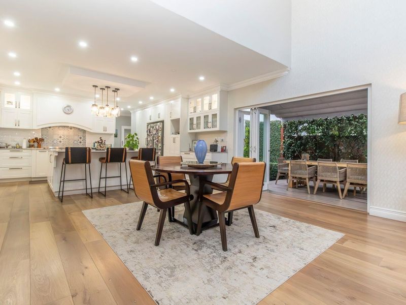 Spacious open-plan kitchen and dining area featuring high-end cabinetry, hardwood floors, and seamless indoor-outdoor flow through large bi-fold doors to the patio.