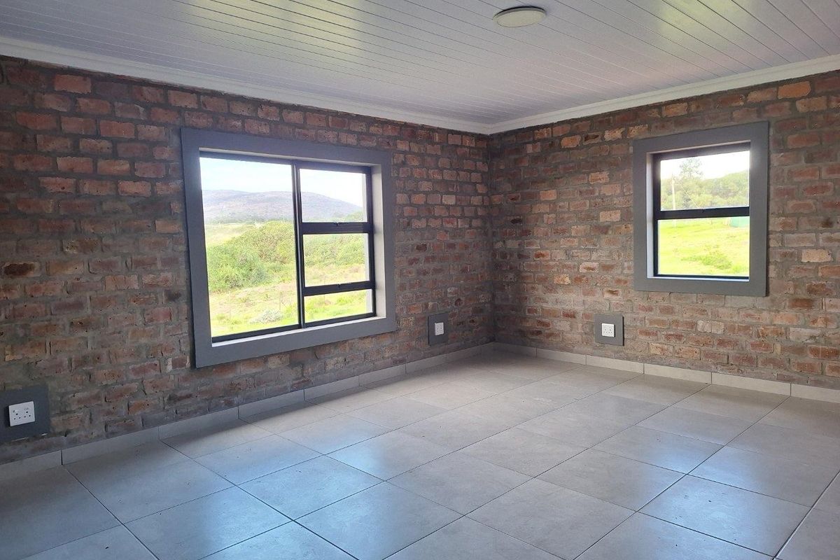 A bright, empty bedroom featuring exposed brick walls, tiled flooring, and large windows offering scenic landscape views.