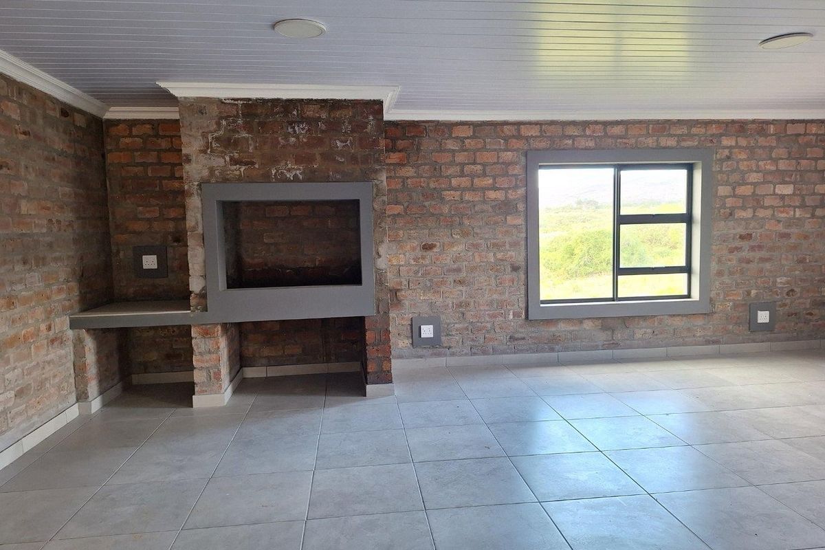 Spacious living area featuring exposed brick walls, a built-in indoor braai fireplace, tiled flooring, and large windows with scenic views.