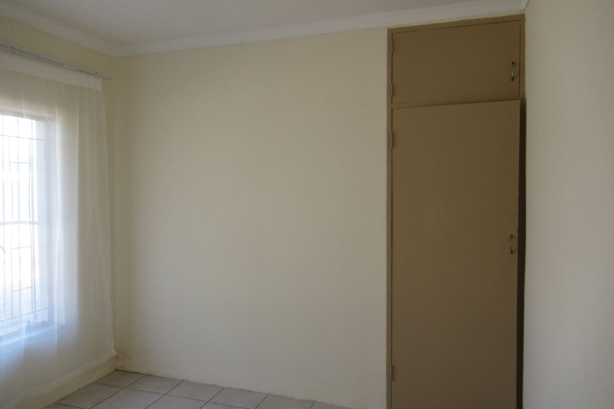 A simple bedroom featuring tiled flooring, a built-in cupboard with overhead storage, and a window with security bars.