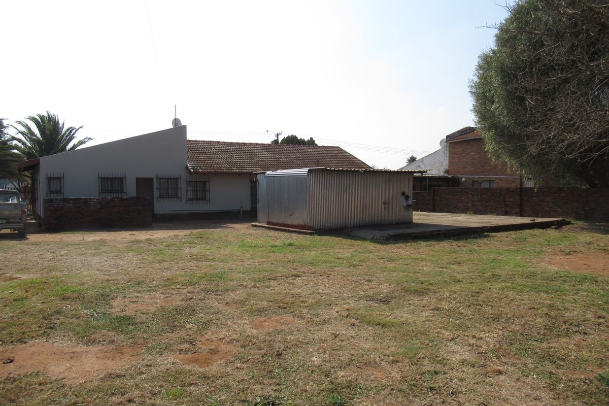 A view of the rear exterior of the property featuring a large yard, a brick boundary wall, and a detached corrugated metal storage structure.