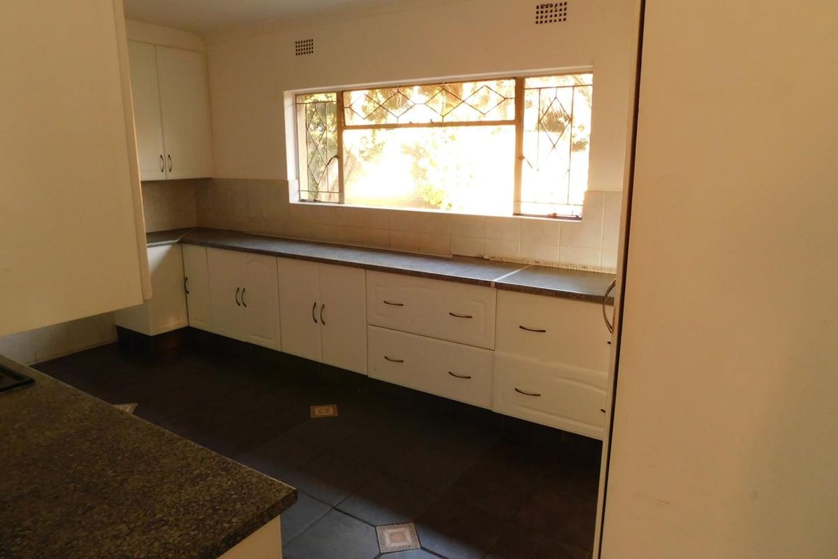 A functional kitchen featuring white built-in cabinetry, stone countertops, and dark tiled flooring with a large window providing natural light.