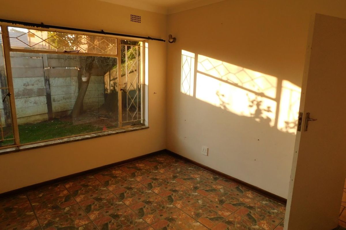 An empty bedroom featuring tiled flooring and large steel-framed windows with security bars, offering a blank canvas for renovation.
