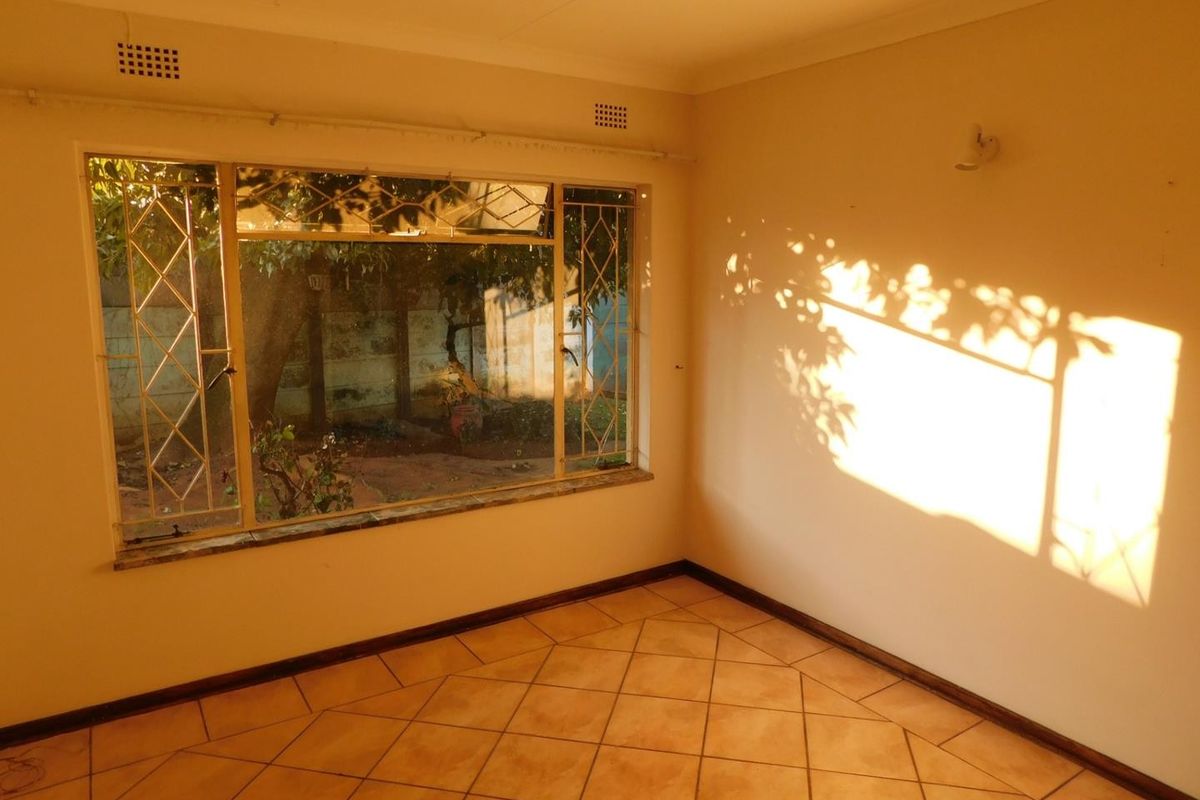 A bright, empty living room featuring tiled flooring and large windows with security bars, offering a clean canvas for interior design.