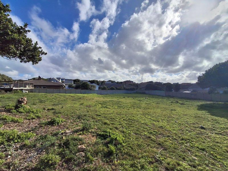 A vacant residential plot of land featuring perimeter boundary walls and established grass coverage, situated in a developed suburban neighborhood.