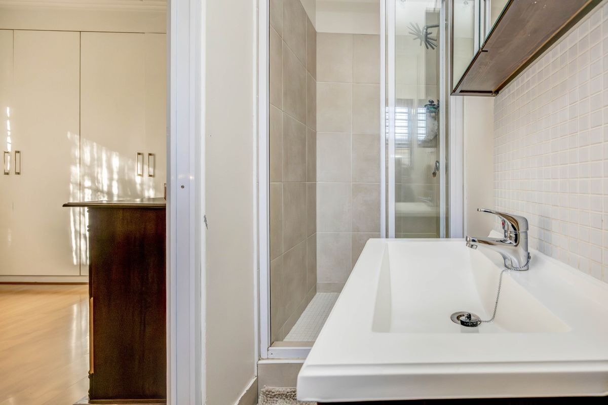 A compact bathroom featuring a modern white vanity basin, tiled shower enclosure, and adjacent built-in wardrobe storage.