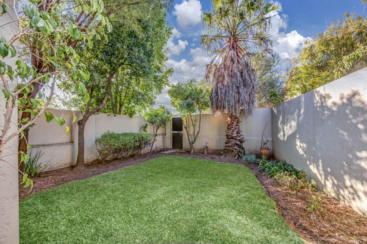 A private rear garden featuring a manicured lawn, established trees, and high boundary walls providing a secluded outdoor space.