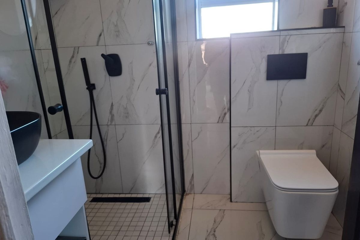 Modern bathroom featuring marble-look wall tiles, a glass-enclosed shower with black fixtures, and a wall-mounted toilet with a concealed cistern.