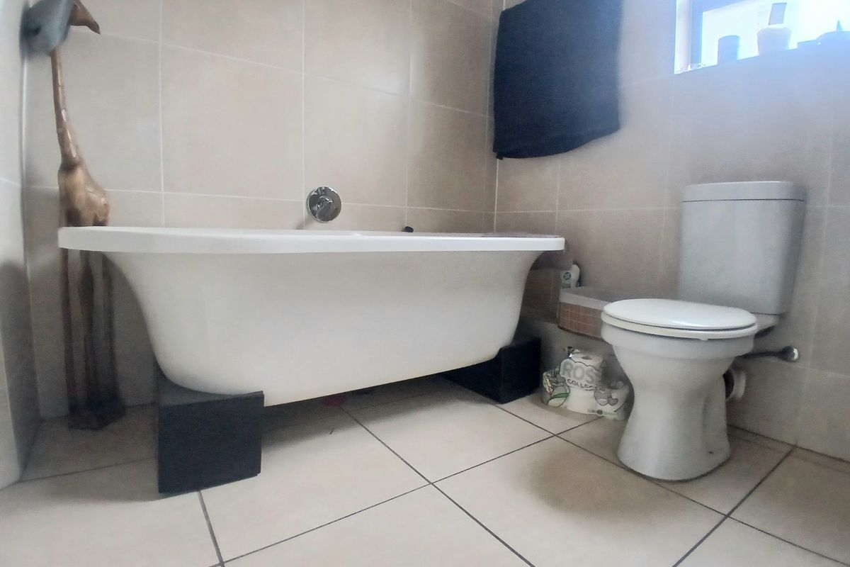 A bathroom featuring a freestanding bathtub with custom support blocks, a standard toilet, and neutral wall tiling.