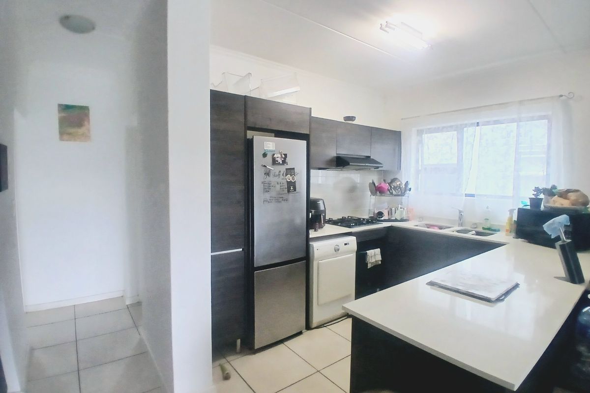 A functional kitchen featuring dark cabinetry, a breakfast bar, built-in hob, extractor fan, and tiled flooring, adjacent to a hallway entrance.