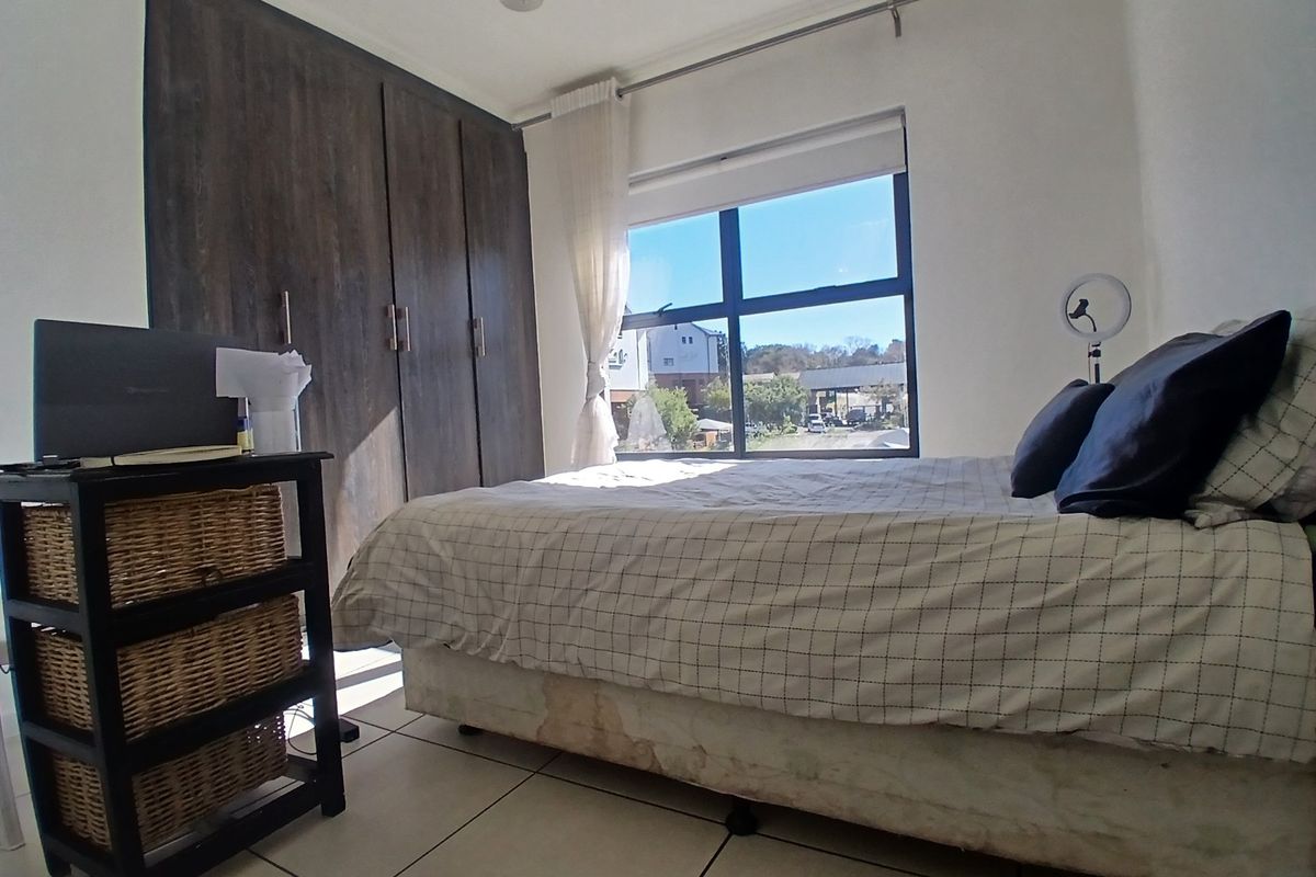 A bedroom featuring built-in dark wood-look cupboards, tiled flooring, and a large window providing natural light and an exterior view.