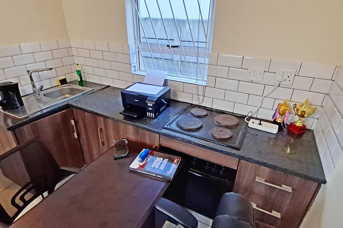 Compact kitchen featuring dark cabinetry, granite-look countertops, white subway tile backsplash, stainless steel sink, and a built-in electric hob and oven.