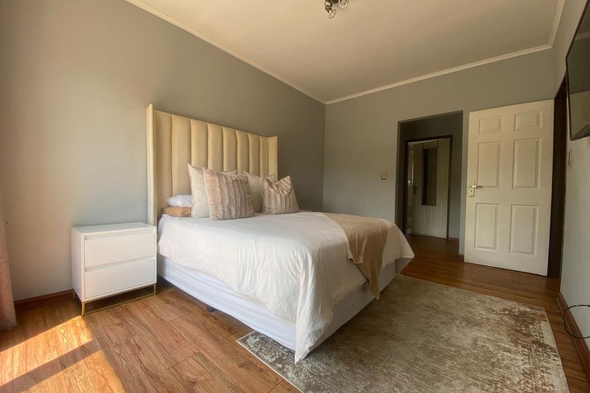 A well-maintained bedroom featuring wood-look flooring, neutral wall tones, and a classic panel door leading to an adjacent space.