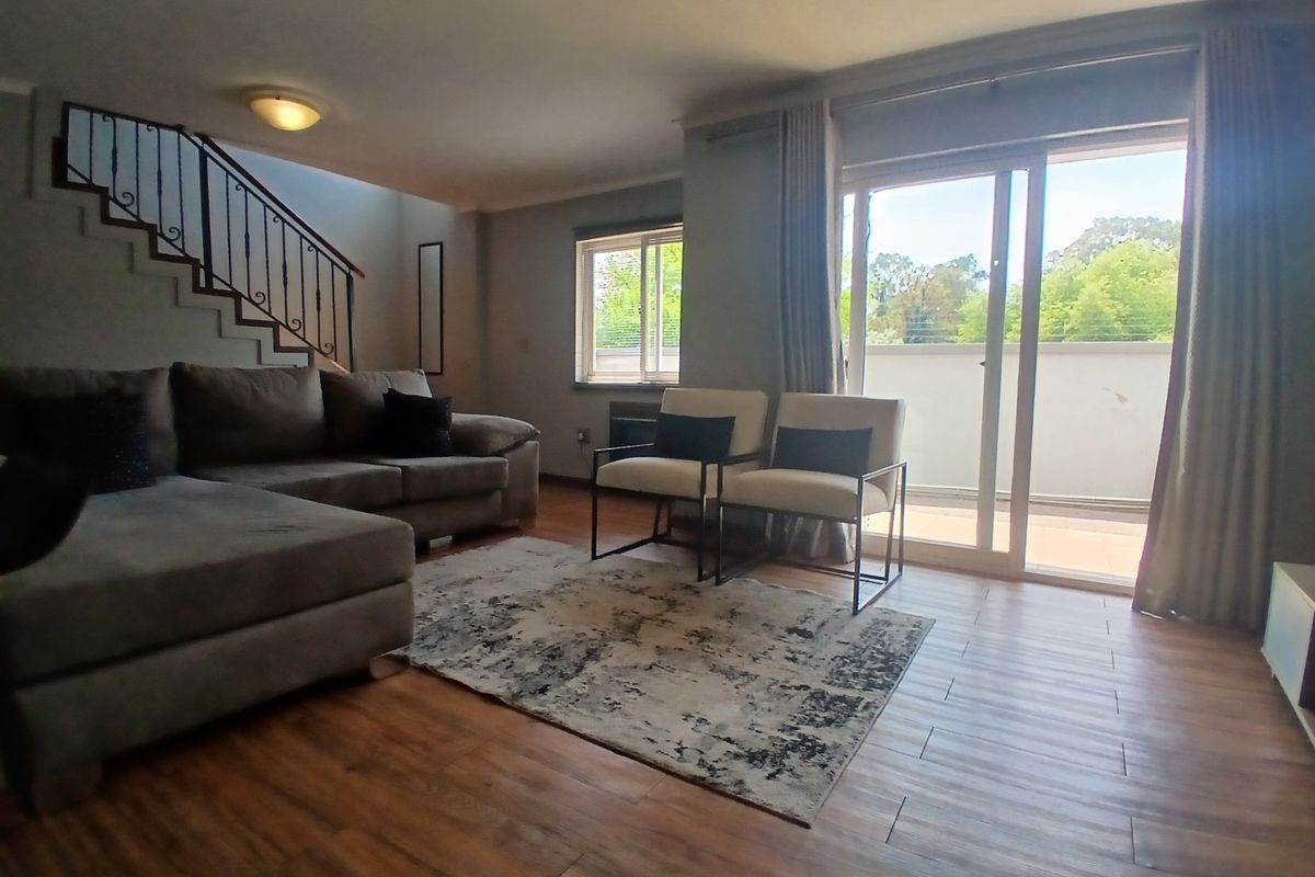Spacious living room featuring wood-look flooring, a staircase with wrought iron railing, and large sliding glass doors providing access to an outdoor balcony area.