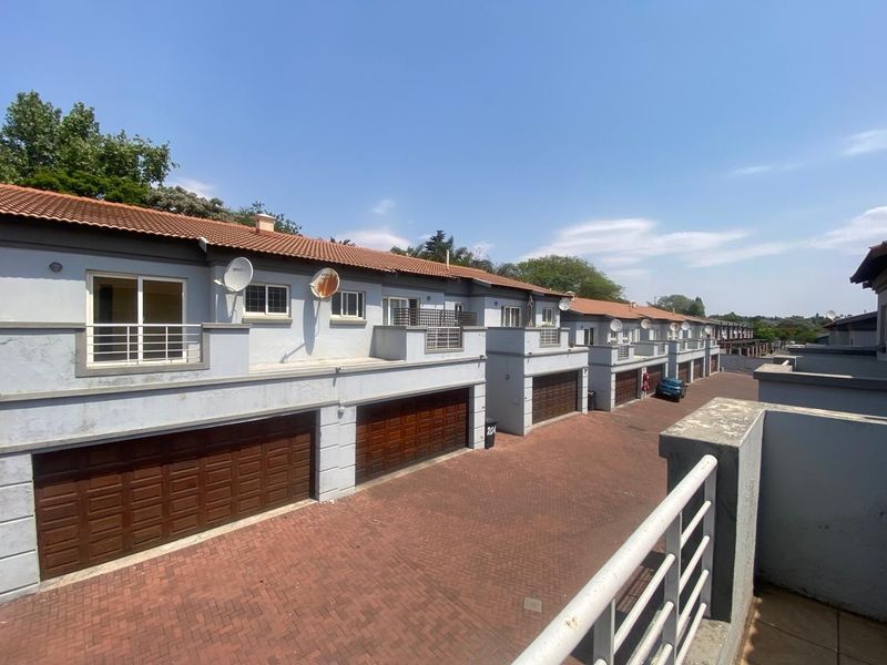 Exterior view of a townhouse complex featuring a paved driveway, multiple garage doors, and upper-level balconies with metal railings.