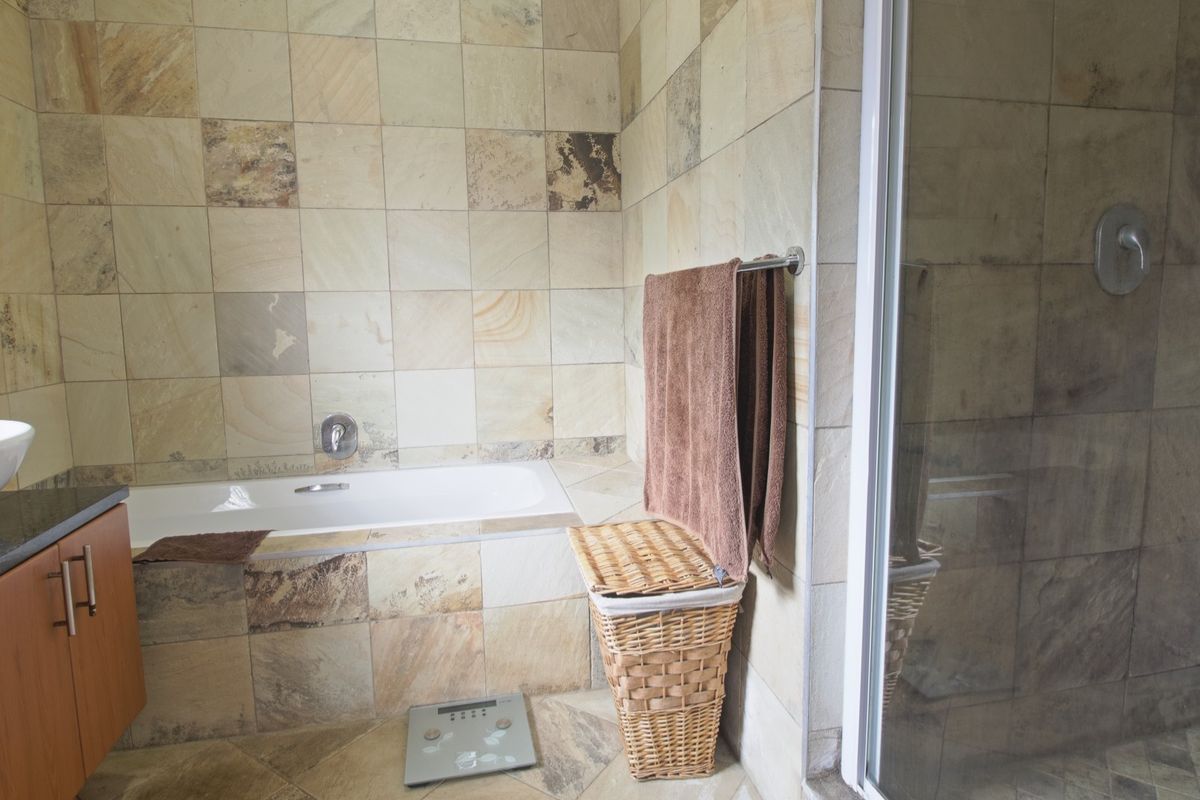 A bathroom featuring natural stone wall and floor tiles, a built-in bathtub, a separate shower enclosure, and a vanity with a vessel sink.