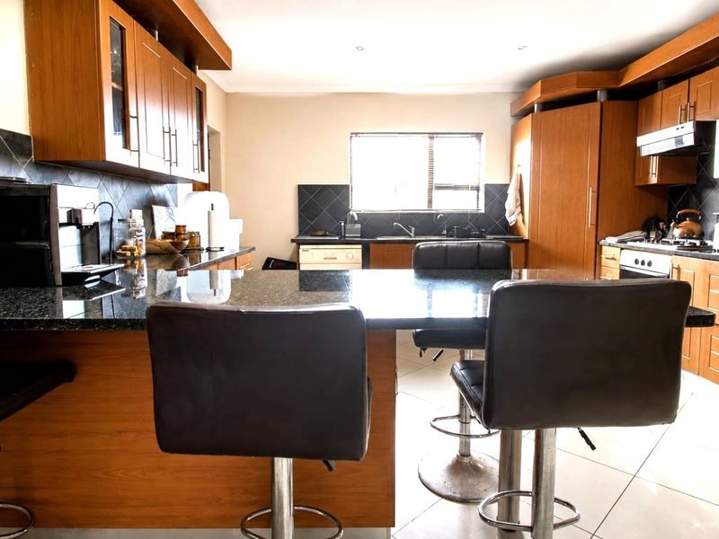 Spacious kitchen featuring wooden cabinetry, granite countertops, a gas hob, and a central breakfast island, providing a functional and well-equipped cooking space.