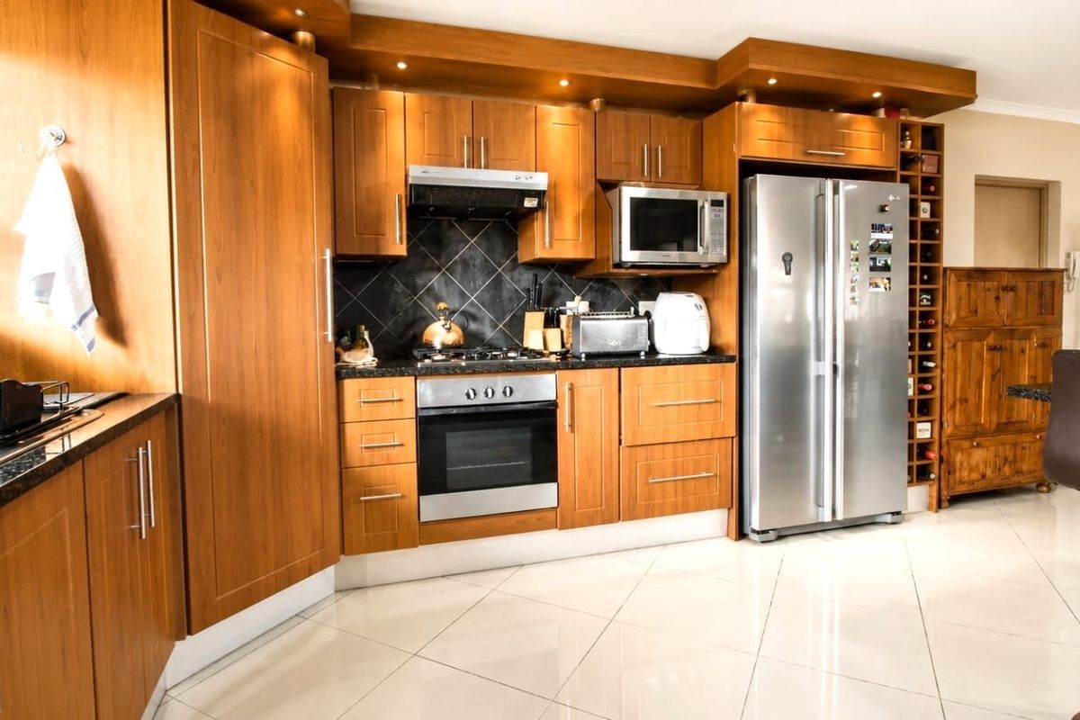 A well-maintained kitchen featuring warm wood cabinetry, granite countertops, integrated appliances, and polished tile flooring with a built-in wine rack.