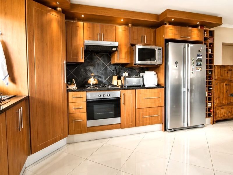 A well-maintained kitchen featuring warm wood cabinetry, granite countertops, integrated appliances, and polished tile flooring with a built-in wine rack.