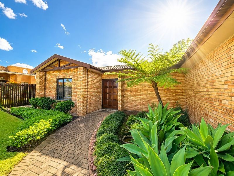 A well-maintained face brick front facade featuring a paved walkway leading to a timber entrance door, surrounded by established landscaped gardens.