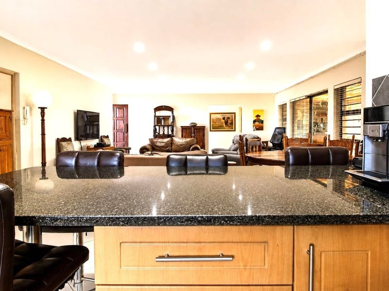 Spacious open-plan living area featuring a kitchen island with granite countertops and wooden cabinetry, flowing into a comfortable lounge and dining space.