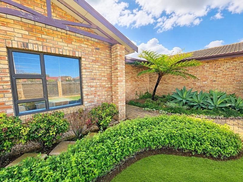 A well-maintained rear exterior view featuring a face brick facade, paved garden pathways, and established landscaping.