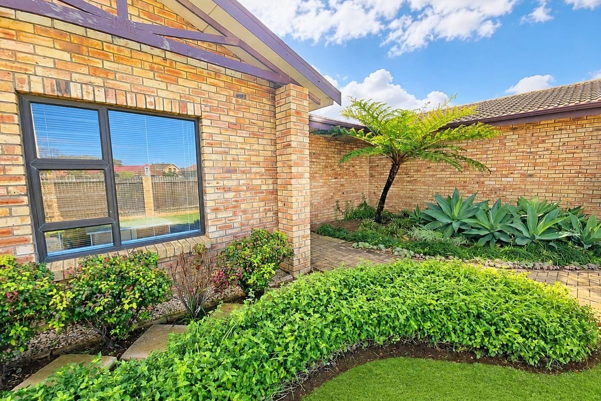 A well-maintained rear exterior view featuring a face brick facade, paved garden pathways, and established landscaping.