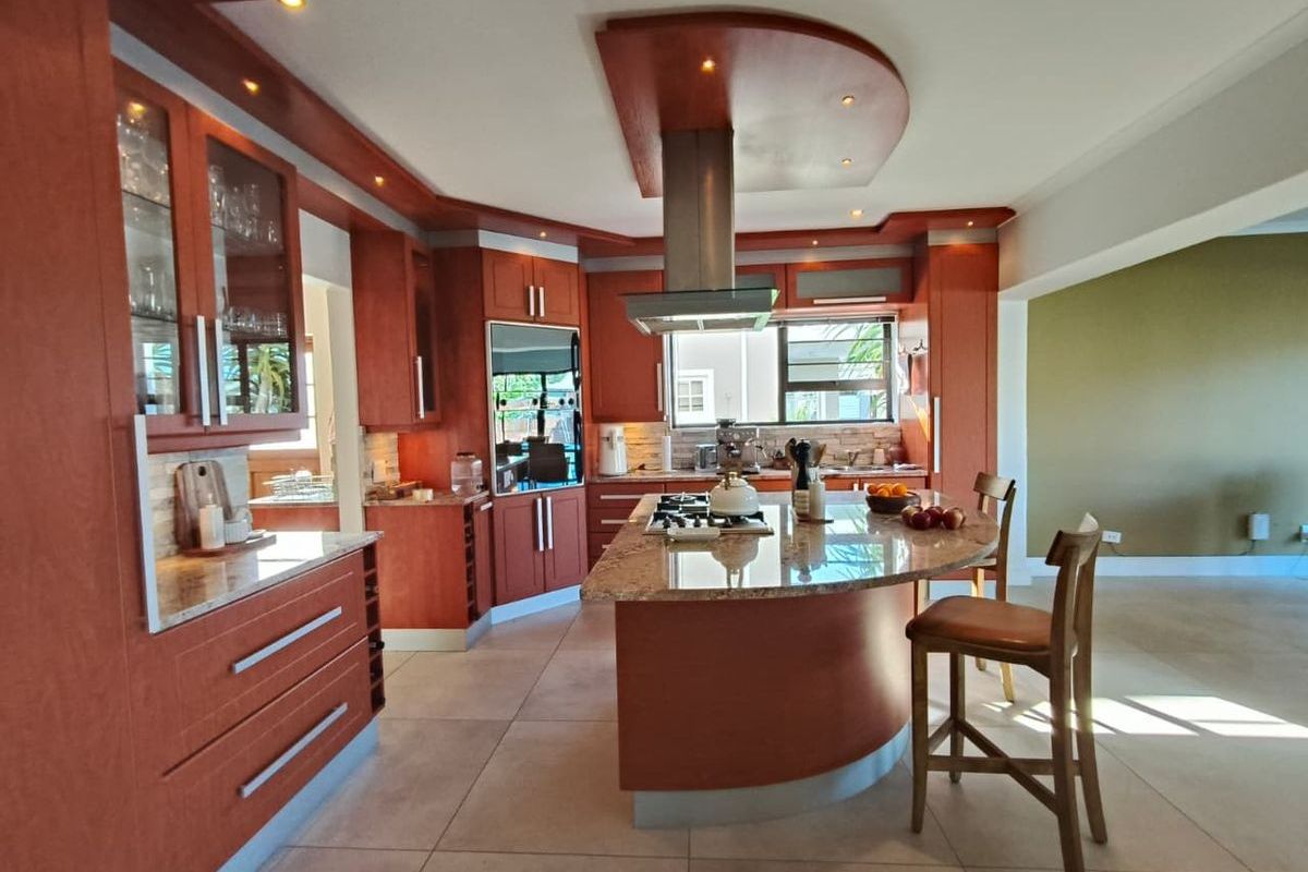 Spacious kitchen featuring warm-toned cabinetry, a central island with a built-in gas hob, granite countertops, and a modern stainless steel extractor fan.