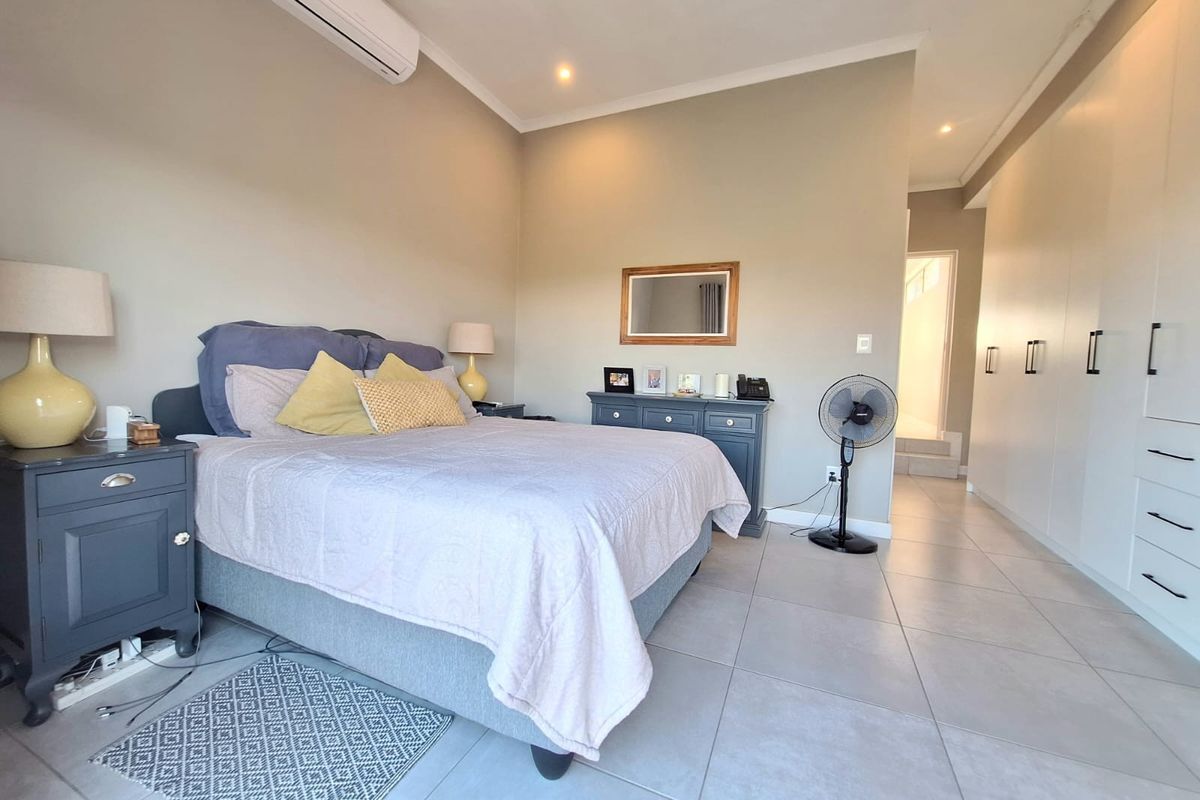 Spacious bedroom featuring neutral tiled flooring, built-in floor-to-ceiling cabinetry, and a wall-mounted air conditioning unit.