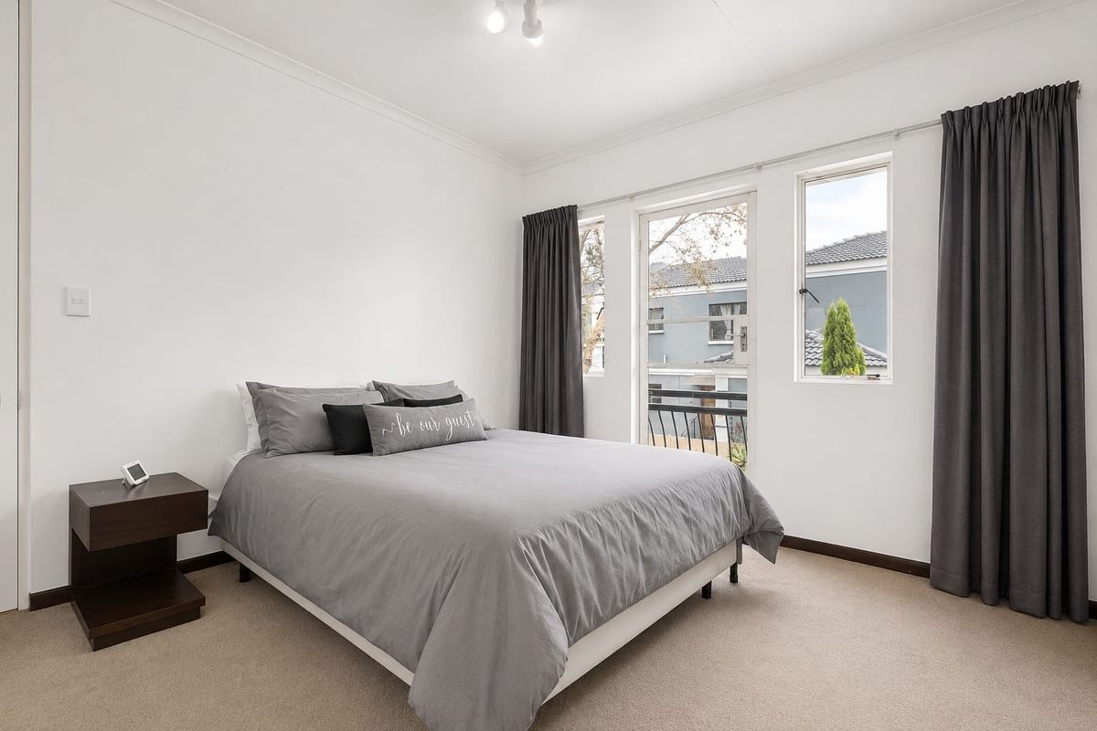 A well-maintained bedroom featuring neutral carpeting, coved ceilings, and a glass door providing access to a private balcony.