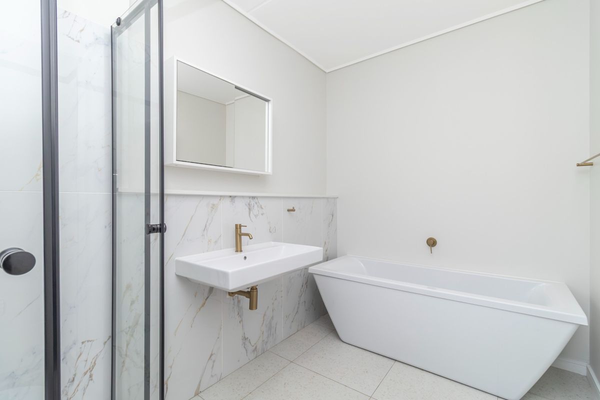 Modern bathroom featuring a freestanding bathtub, wall-mounted basin with brass fixtures, and marble-look tiled walls.