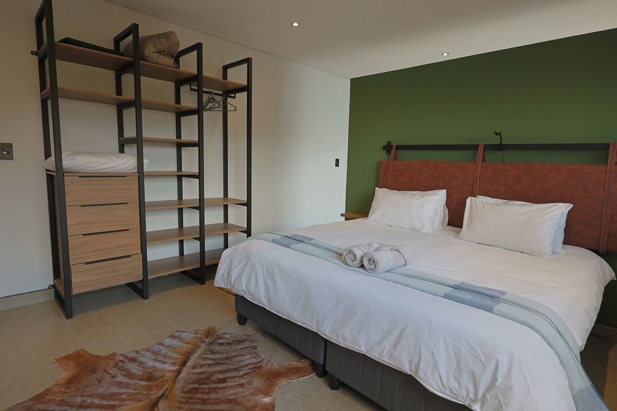 A modern bedroom featuring a green accent wall, recessed ceiling lighting, and polished concrete flooring.