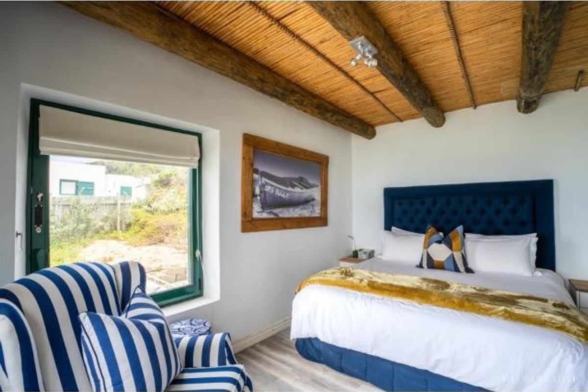 A cozy bedroom featuring a rustic exposed timber and reed ceiling, large window with garden views, and neutral flooring.