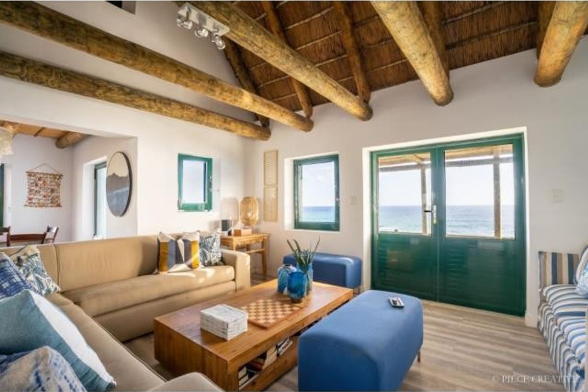 Bright living area featuring exposed timber rafters, a thatched ceiling, and double doors opening to a scenic coastal view.