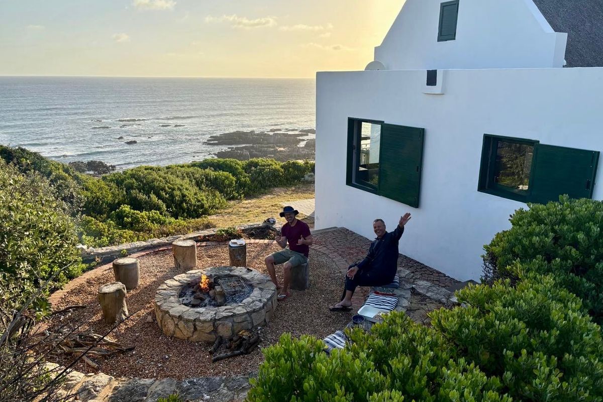 A scenic outdoor patio area featuring a stone-built fire pit, overlooking the ocean with direct access to the rear of the farmhouse.