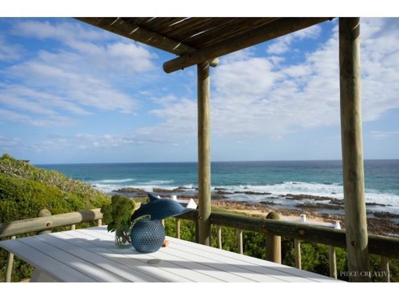 A covered wooden patio offering expansive, elevated views of the coastline and ocean, featuring rustic timber structural supports.