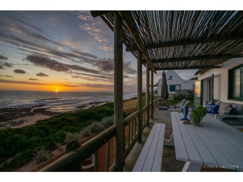 A scenic covered patio overlooking the ocean at sunset, featuring rustic timber support beams and stone flooring.