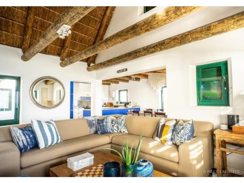 A bright open-plan living area featuring a high vaulted thatched ceiling with exposed timber beams, connecting seamlessly to the kitchen and dining space.