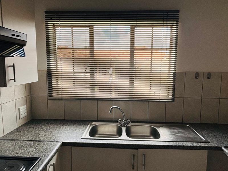 A functional kitchen area featuring a double stainless steel sink, granite-look countertops, tiled backsplash, and built-in cabinetry with an integrated extractor fan.