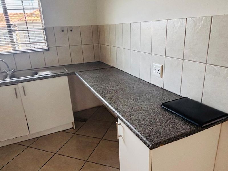 A functional kitchen area featuring granite-look laminate countertops, tiled splashbacks, a stainless steel sink, and white cabinetry with tiled flooring.