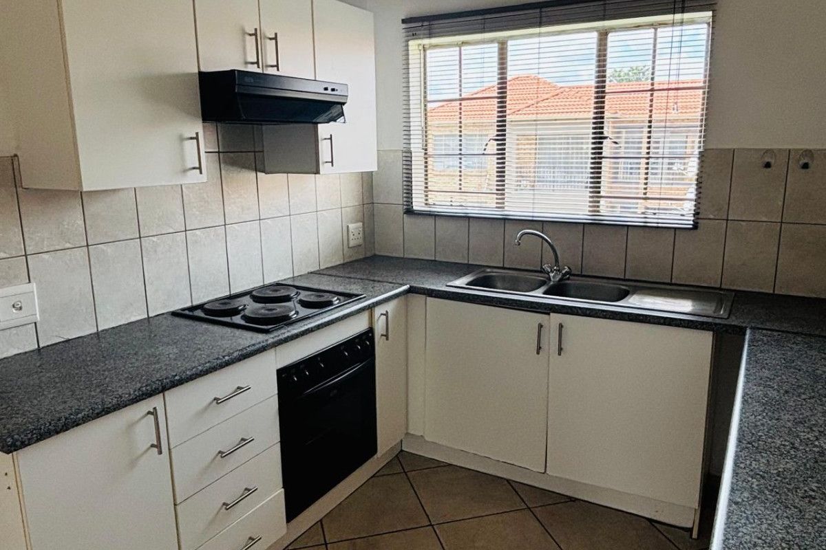 A functional kitchen featuring white cabinetry, granite-look countertops, a built-in oven, electric hob, extractor fan, and a double-basin sink with tiled splashbacks.