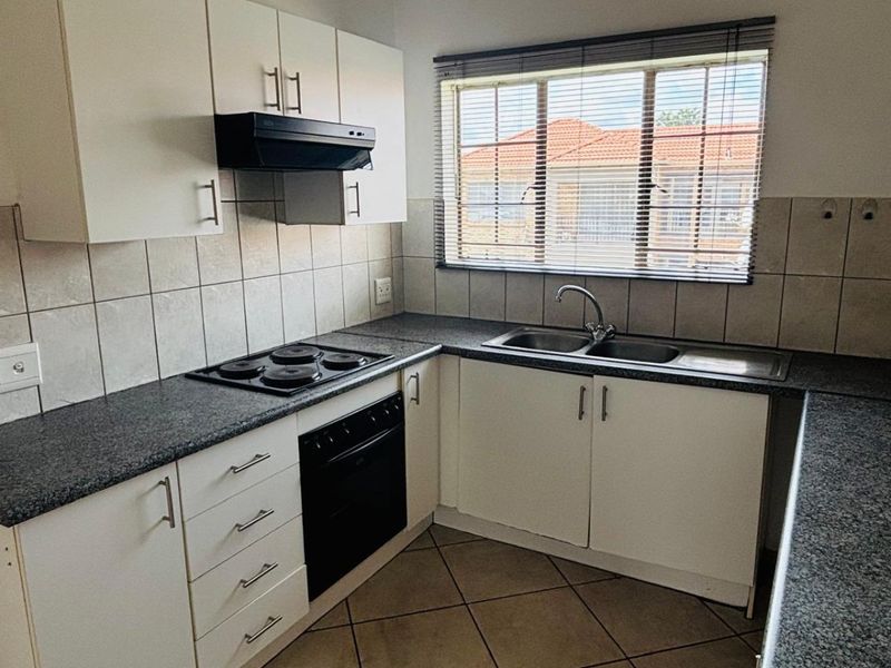 A functional kitchen featuring white cabinetry, granite-look countertops, a built-in oven, electric hob, extractor fan, and a double-basin sink with tiled splashbacks.