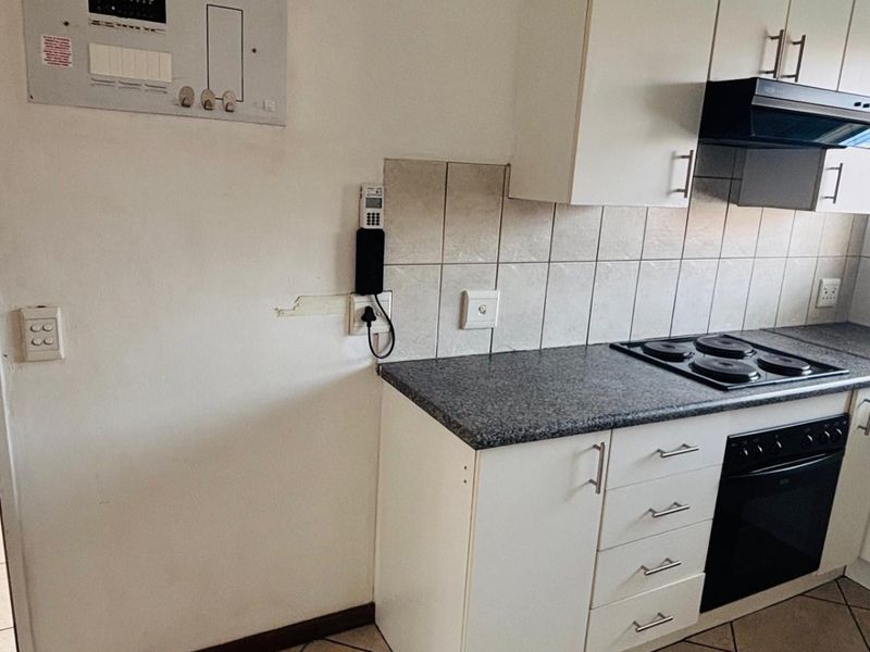 A functional kitchen area featuring white cabinetry, a dark granite-look countertop, built-in oven, hob, and extractor fan, with tiled flooring throughout.