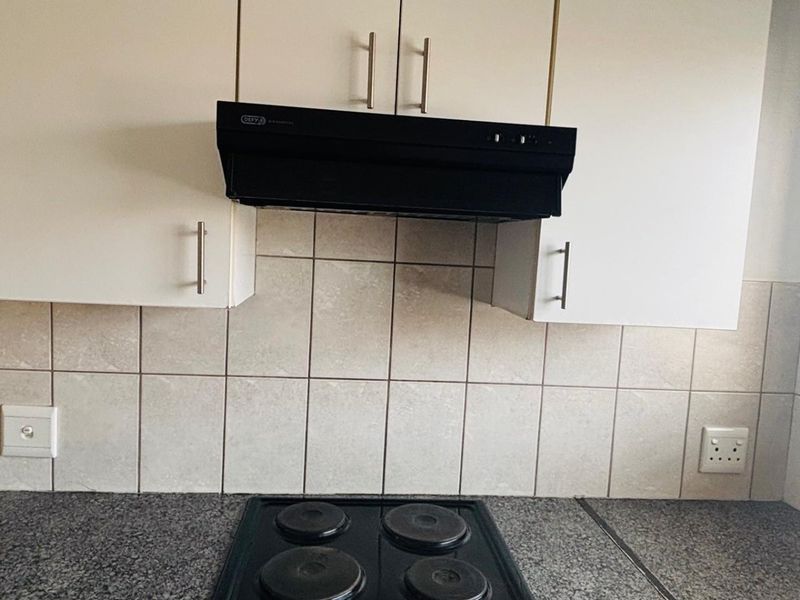 A functional kitchen area featuring a granite-look countertop, a four-plate electric hob, and a black extractor fan with white overhead cabinetry.