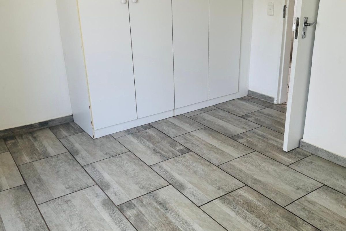 A bright, empty bedroom featuring modern wood-look floor tiles and built-in white cabinetry.