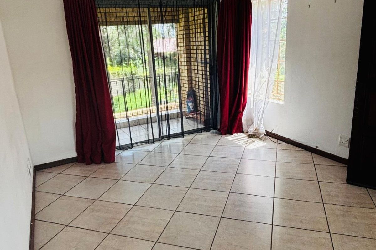 An empty living room featuring tiled flooring, sliding glass doors leading to a balcony, and natural light.